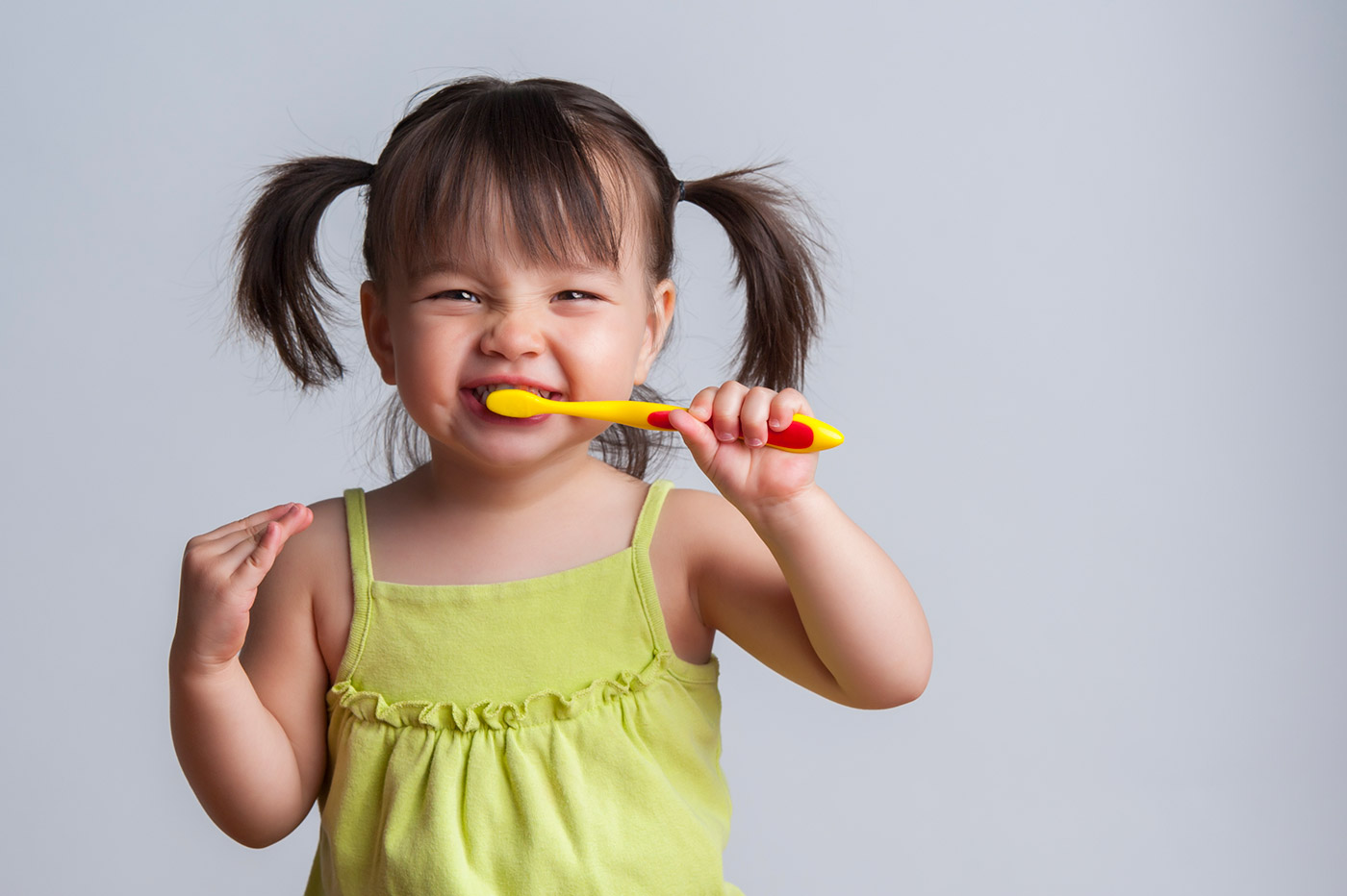 Primera visita al dentista, niña con coletas muy graciosa simulando que se cepilla los dientes